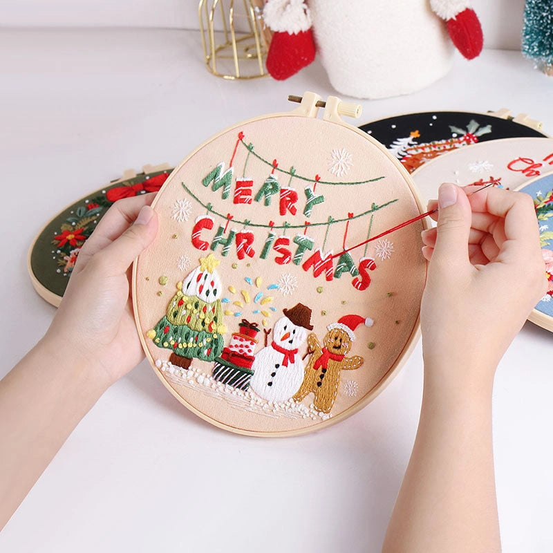 Embroidery hoop with Christmas-themed design being worked on, featuring text and festive elements.