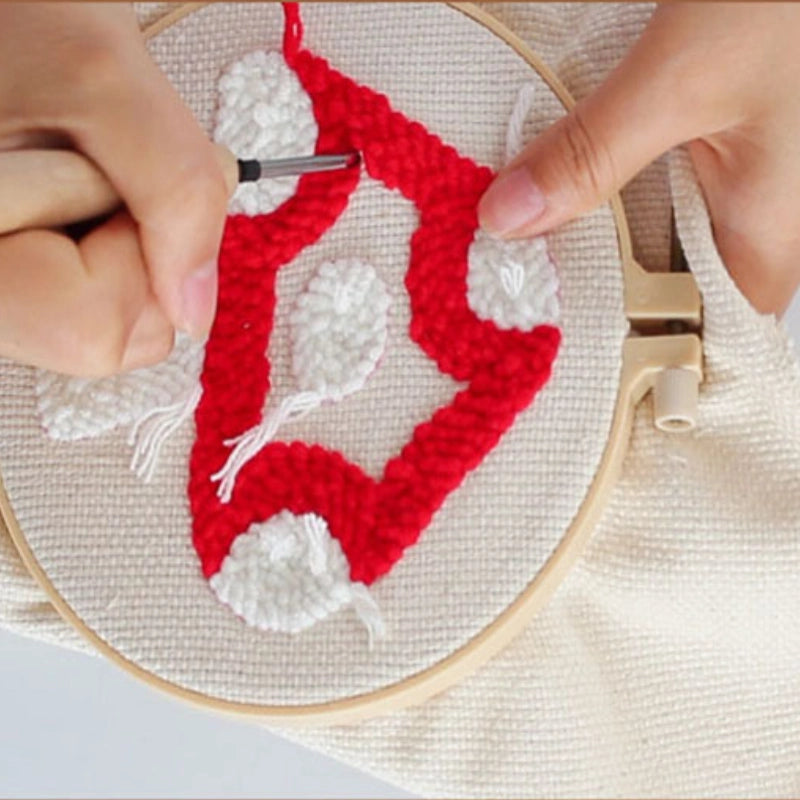 Embroidery hoop with red and white pattern being worked on.