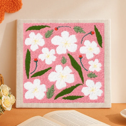 This delightful punch needle piece features white blossoms scattered across a soft pink background, paired with green leaves and tiny red buds.