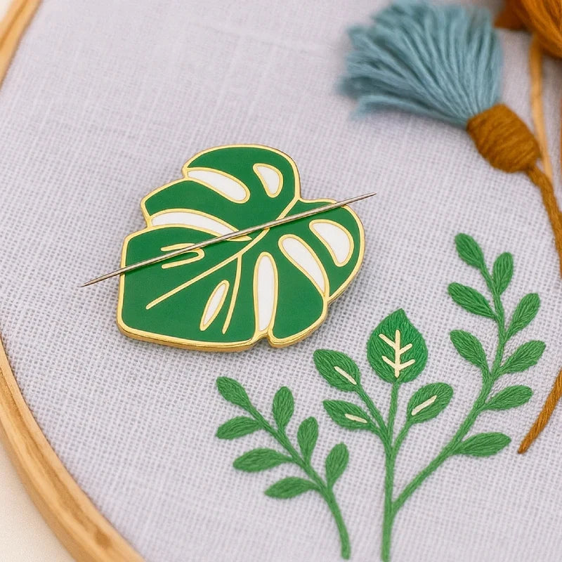 Green leaf-shaped brooch on a white fabric background with embroidery