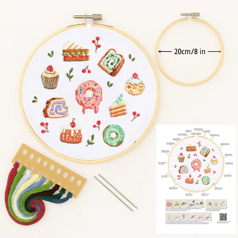 Embroidery hoop with pre-designed pattern of pastries, colorful threads, needles, and a chart on a white background.