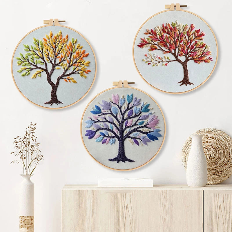 Three embroidered tree designs in hoops on a white wall with decorative vases.