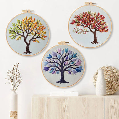 Three embroidered tree designs in hoops on a white wall with decorative vases.