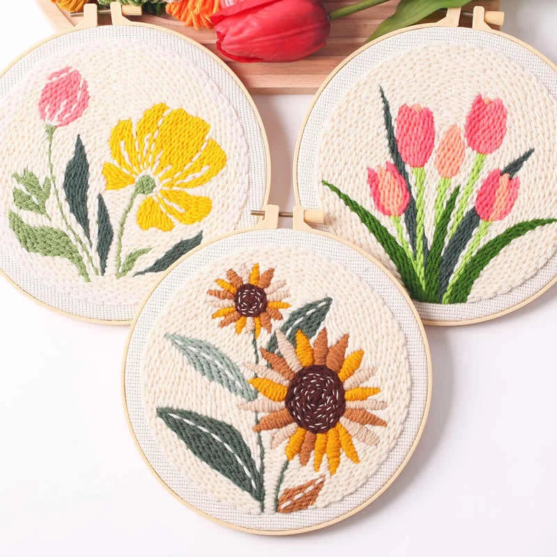 Three embroidered floral designs in wooden hoops on a white background