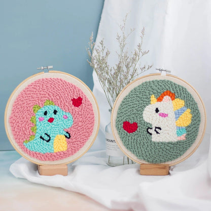 Two embroidered hoop art pieces with a dinosaur and unicorn design on a light blue background.