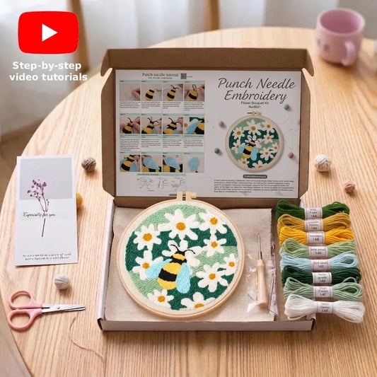 Punch needle embroidery kit with bee and flower design, thread skeins, and tools on a wooden table.