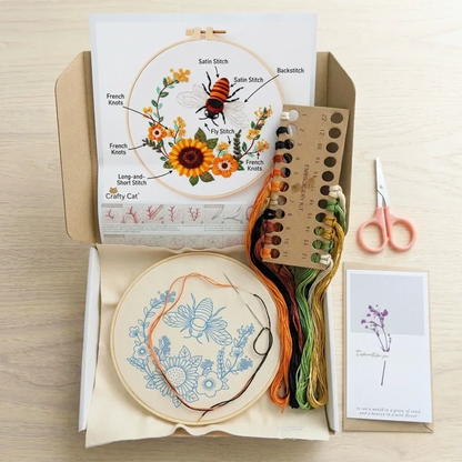 Embroidery kit with hoop, colorful threads, scissors, and pattern featuring a bee and flowers.