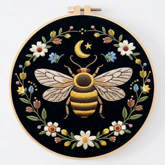 Hand-embroidered bee and celestial moon design in a circular floral wreath on black fabric.
