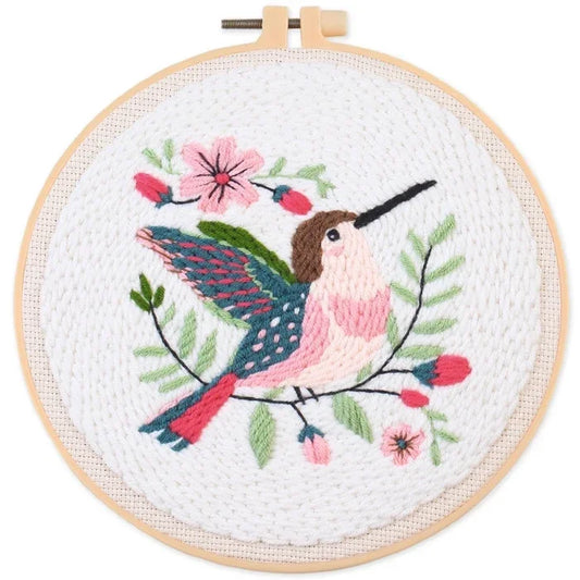 Hand-embroidered hummingbird and pink flowers on white fabric in a wooden hoop