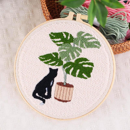 Punch Needle hoop art featuring a black cat sitting next to a potted monstera plant.
