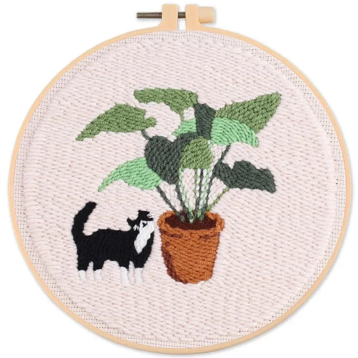 Punch Needle art in a wooden hoop featuring a black and white cat and a potted plant.