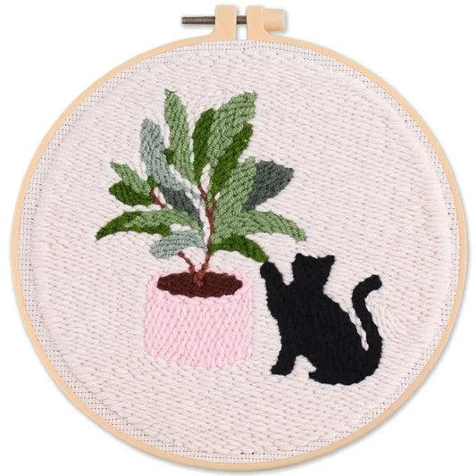 Punch Needle art of a black cat next to a potted green plant in a wooden hoop