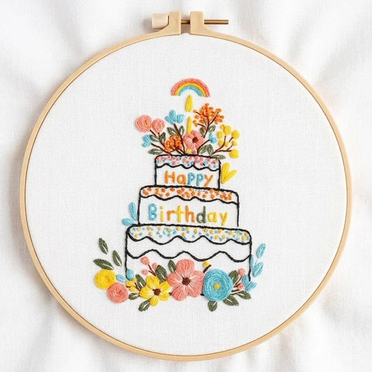 Hand-embroidered birthday cake with flowers and a rainbow in a wooden hoop