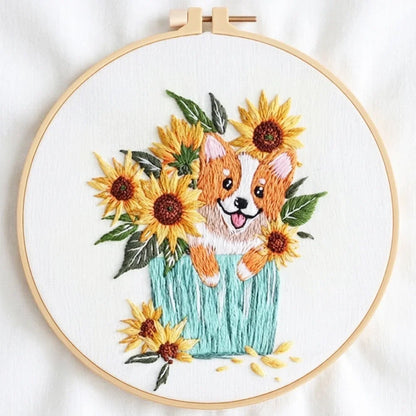 Hand embroidery of a cute corgi puppy peeking out from a bouquet of sunflowers in a blue pot.