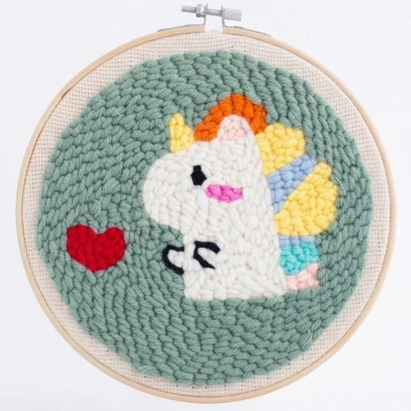 Handmade punch needle embroidery of a white unicorn with a colorful mane and a red heart.