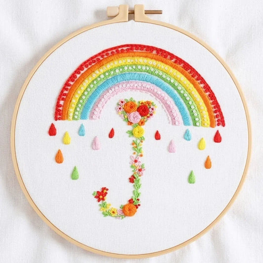 Hand-embroidered rainbow umbrella with floral handle and colorful raindrops in a wooden hoop.