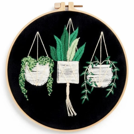 Hand-embroidered hanging plants in pots on a black fabric background in a wooden hoop