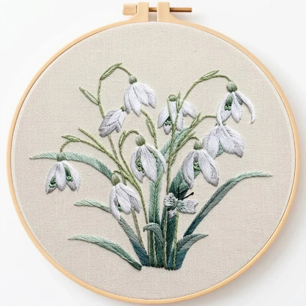 Hand embroidery of white snowdrop flowers with green leaves in a wooden hoop