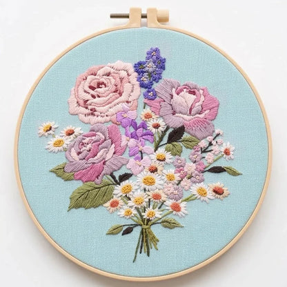 Hand embroidery of a colorful floral bouquet with pink roses and daisies on light blue fabric.
