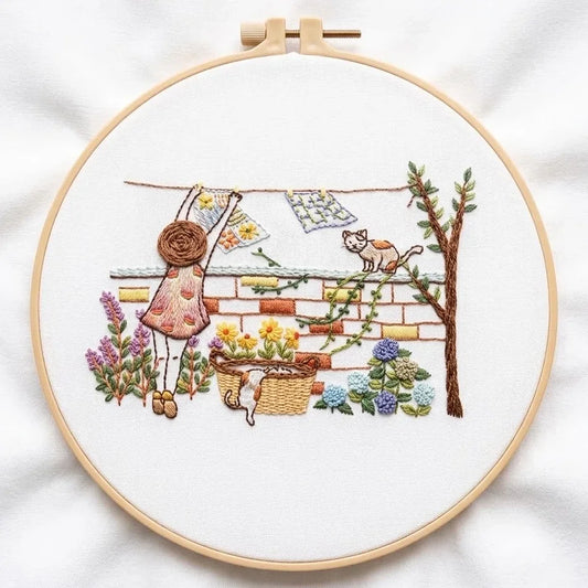Hand embroidery of a girl hanging laundry with cats and flowers in a garden setting.