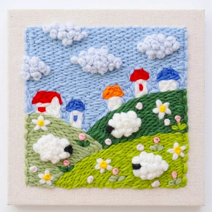 Punch needle embroidery kit featuring a landscape with sheep, houses, and clouds.