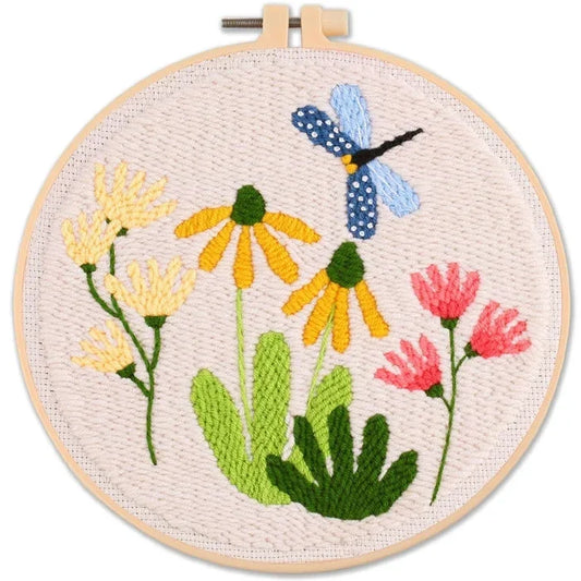 punch needle floral design with yellow and pink flowers and a blue dragonfly in a hoop