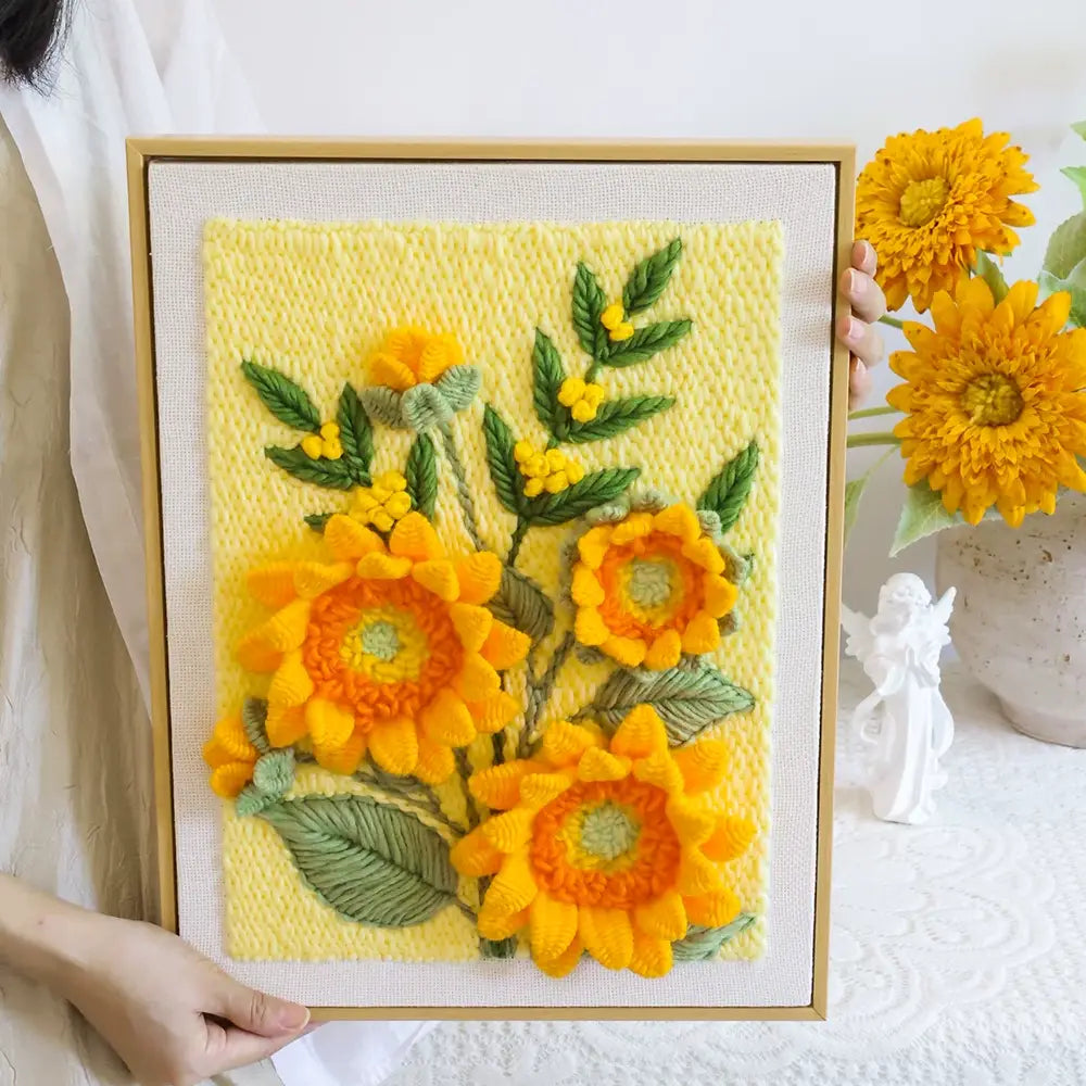 Handmade sunflower punch needle art in a light wood frame against a yellow background.